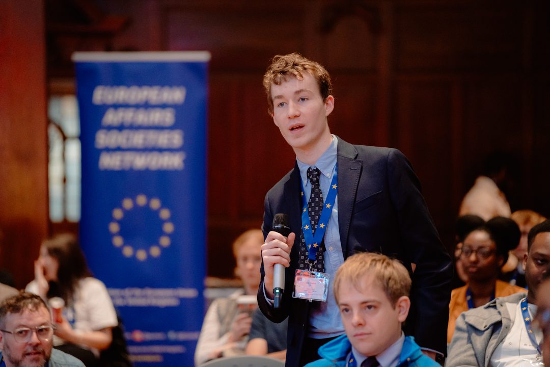 A young delegate speaking at the microphone beside the European Affairs Societies Network banner